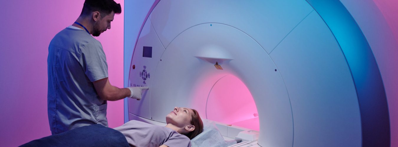 Young doctor pushing button on panel to start mri scan procedure while female patient lying on long table